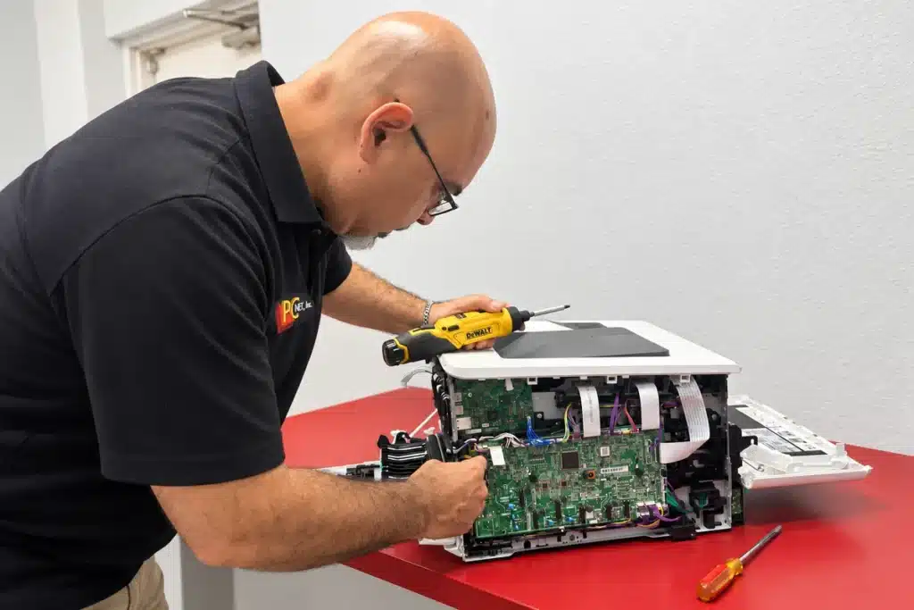 Printer Board Repair – PC Net Miami PC Net technician repairing the main circuit board of an office printer at the Miami repair shop
